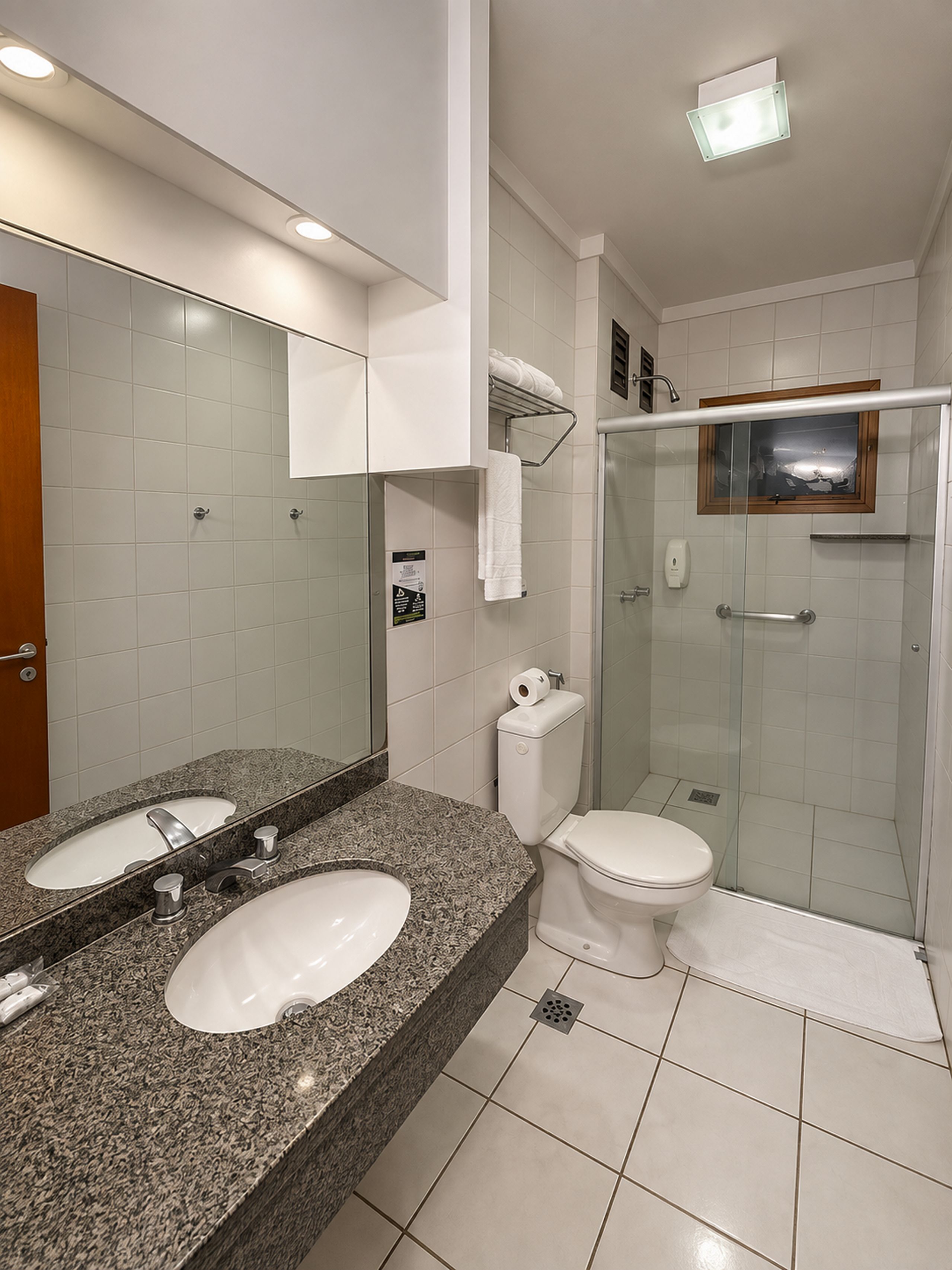 Ein modernes Badezimmer mit einer Naturstein-Arbeitsplatte, zwei Waschbecken, einer Toilette und einer Duschkabine.