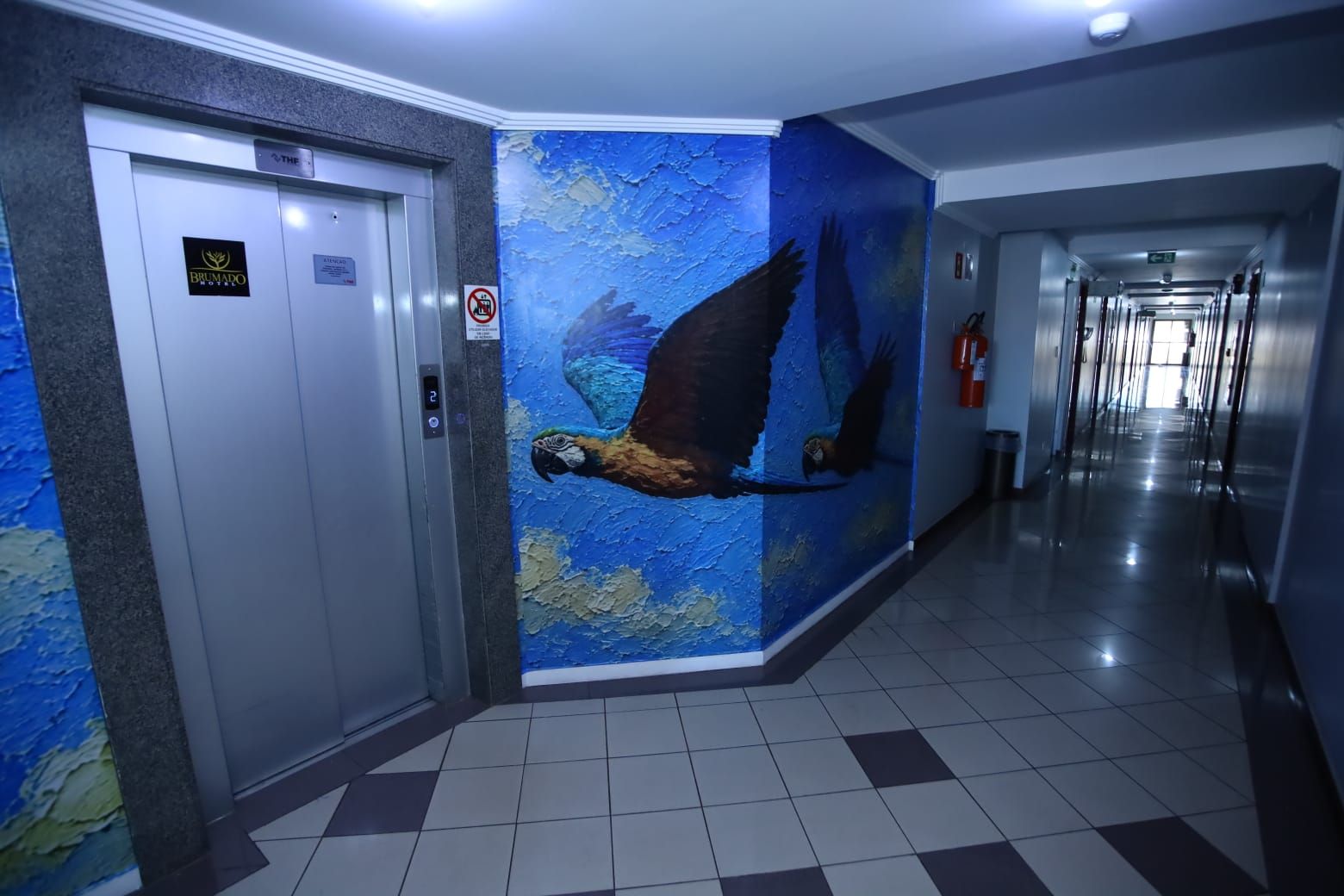 Pasillo de hotel con un mural de un pájaro, un cartel de prohibido fumar y un extintor.