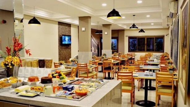 A buffet setup with various food items, multiple dining tables, and chairs. - Brumado Hotel (Campo Grande)