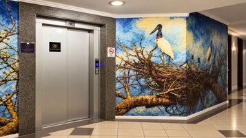 Un ascensor con un letrero de 'No fumar', un botón con el número '6' y un mural en la pared de un pájaro en una rama.