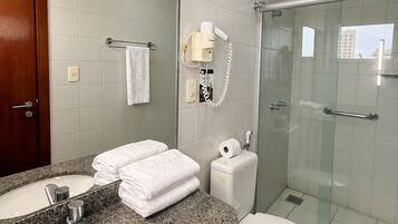 A bathroom with a granite countertop, two sinks, a toilet, a glass shower enclosure, and a towel rack with a white towel.