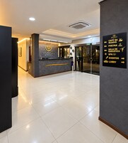 Zona de recepción de hotel con mostrador, cartel con indicaciones hacia las diferentes instalaciones y suelo de baldosas limpias.