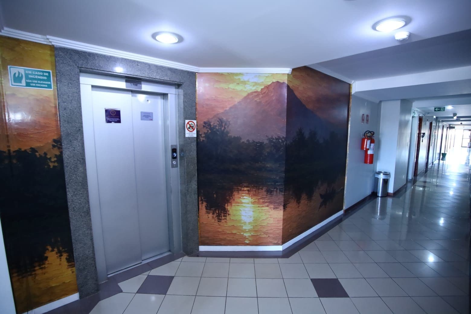 Een gang met een lift, een brandblusser en een muurschildering.