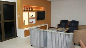 Una sala de estar con televisor, dos sillones, un sofá, una mesa de centro y una pared de madera con estantes.