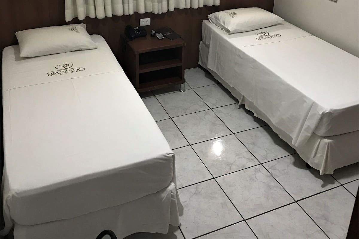 A hotel room with two single beds, a nightstand, a telephone, and an air conditioning unit.