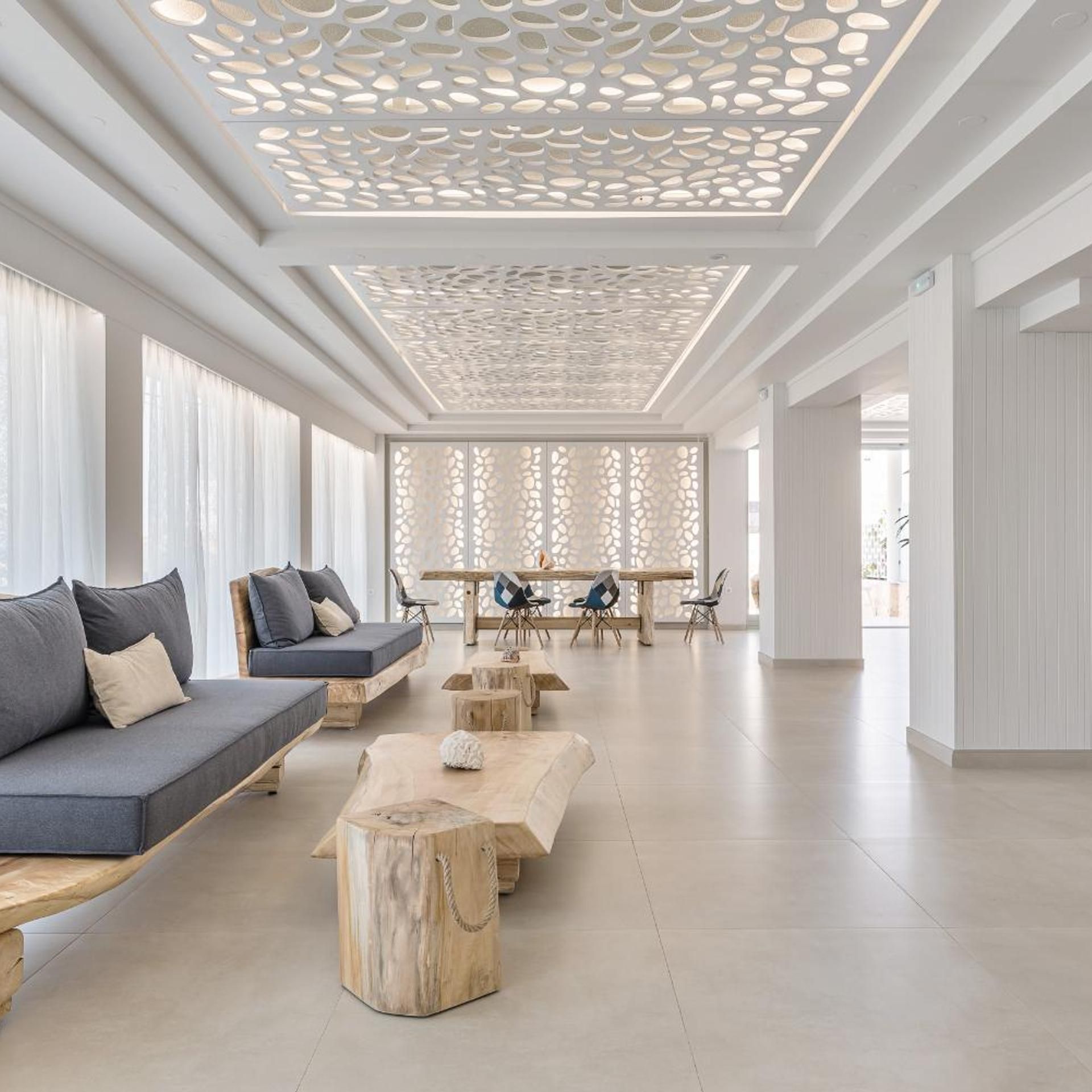 A spacious room with a modern design, featuring a sofa, wooden tables, and a decorative ceiling.