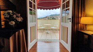 An open door leading to a balcony with a table and chairs, a lamp, and a view of a cityscape. - Hotel Pousada do Arcanjo (Ouro Preto)