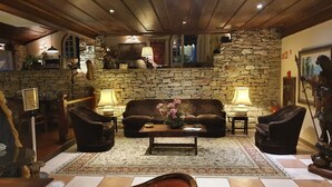 A cozy living room with a stone wall, a brown leather sofa, two armchairs, a coffee table with a vase, and a rug. - Hotel Pousada do Arcanjo (Ouro Preto)