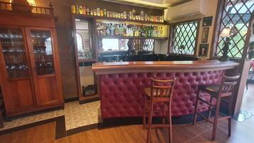 A bar area with a tufted bar counter and stools, a wooden cabinet with glass doors, and shelves with bottles and glasses.