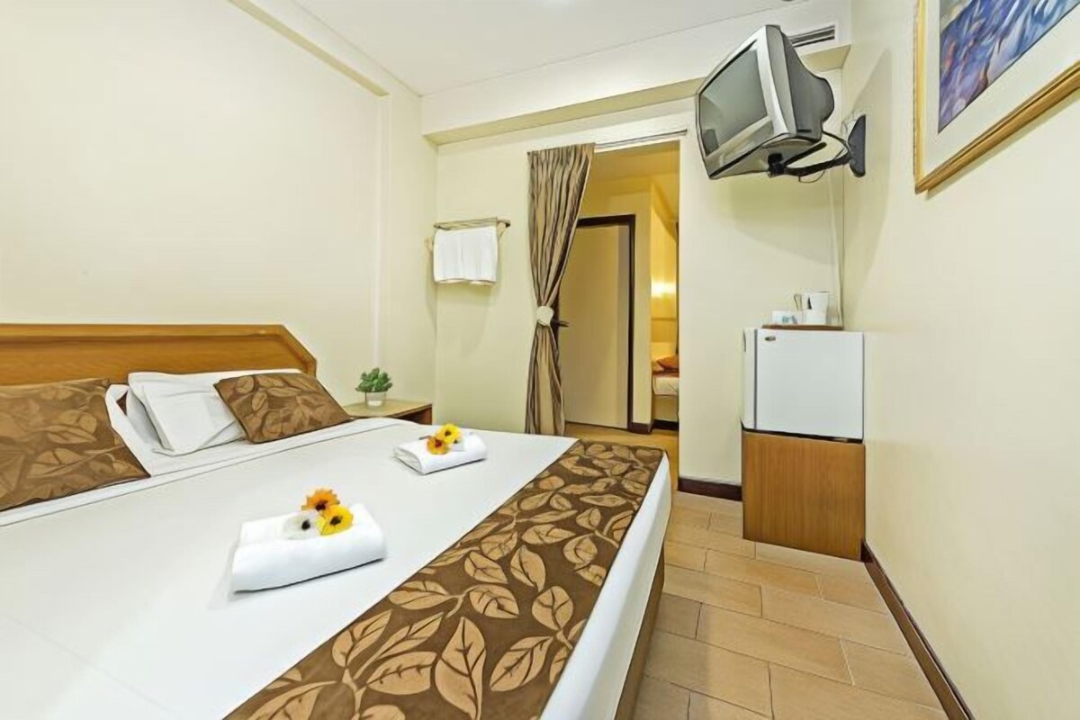 A hotel room with a bed, a television mounted on the wall, a small refrigerator, and a bathroom visible through an open door.
