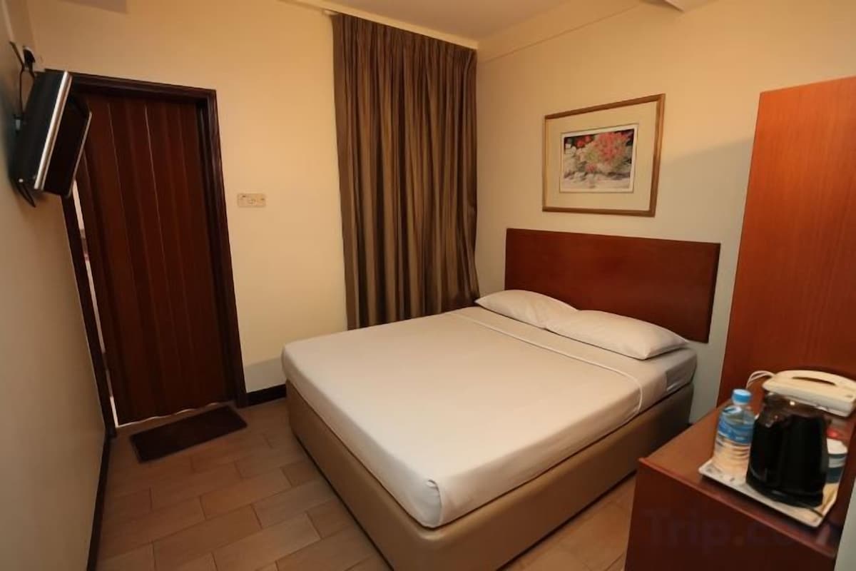 Una habitación de hotel con una cama, un televisor instalado en la pared, una puerta y una ventana con cortinas.