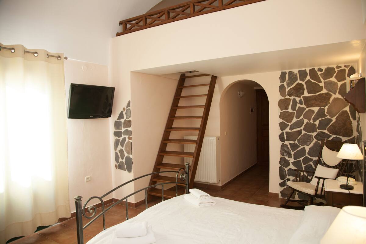 A bedroom with a bed, a wooden ladder, a stone wall, a TV, and a chair.