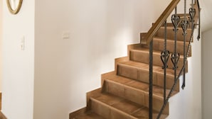 A staircase with a wooden handrail and a wall-mounted light fixture. - Costa Marina Villa (Santorini)