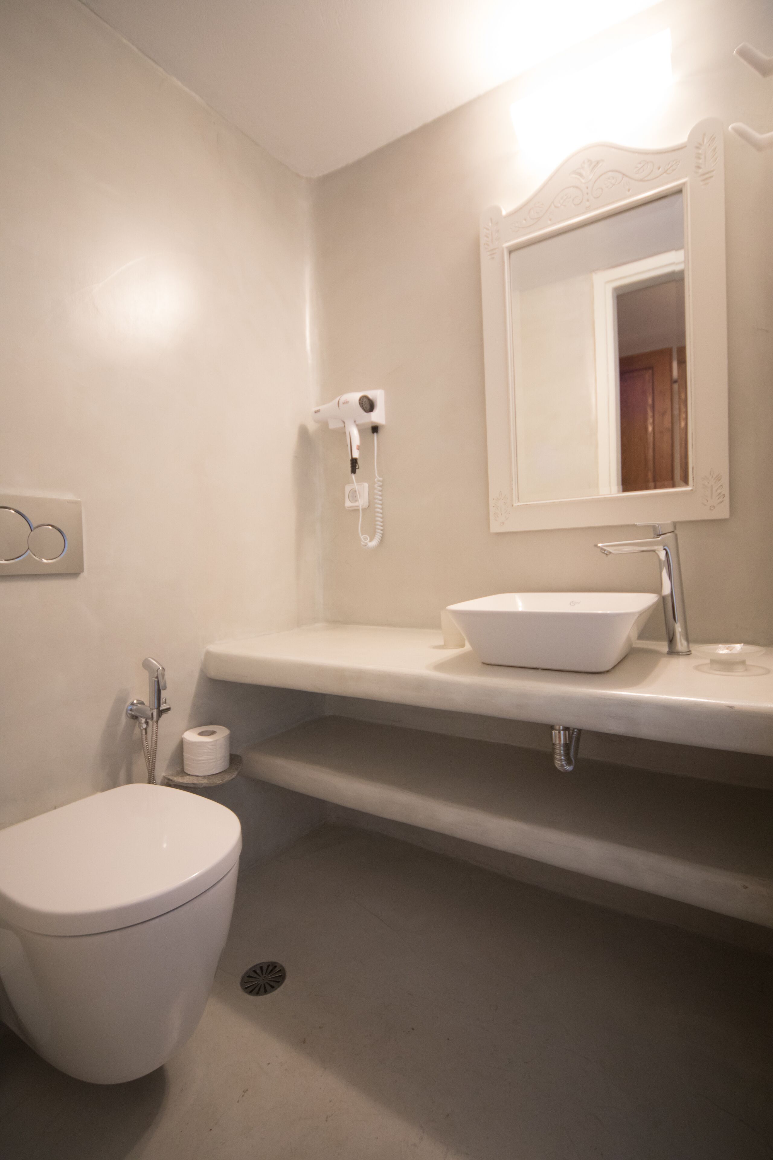 Un baño con inodoro blanco, lavabo con espejo y secador de pelo en la pared.