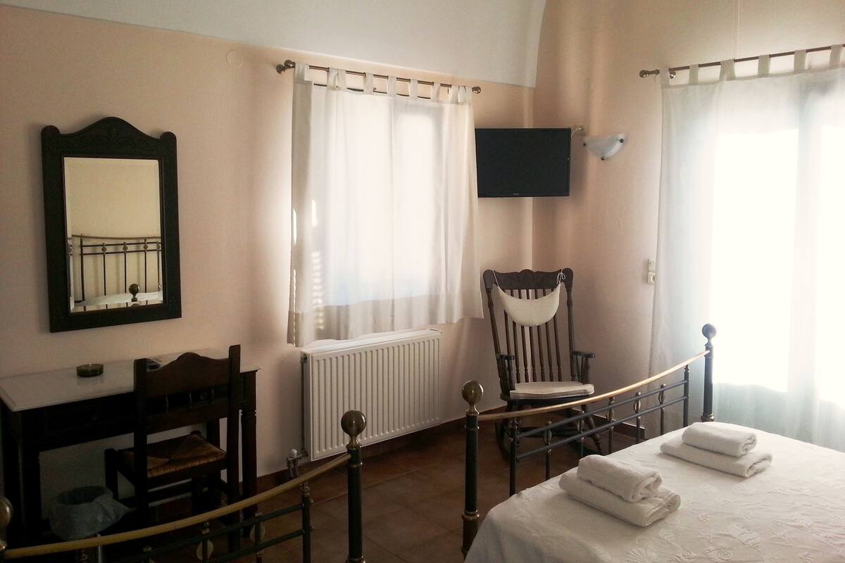 A hotel room with a bed, a chair, a desk, a mirror, a television, and a window with curtains.