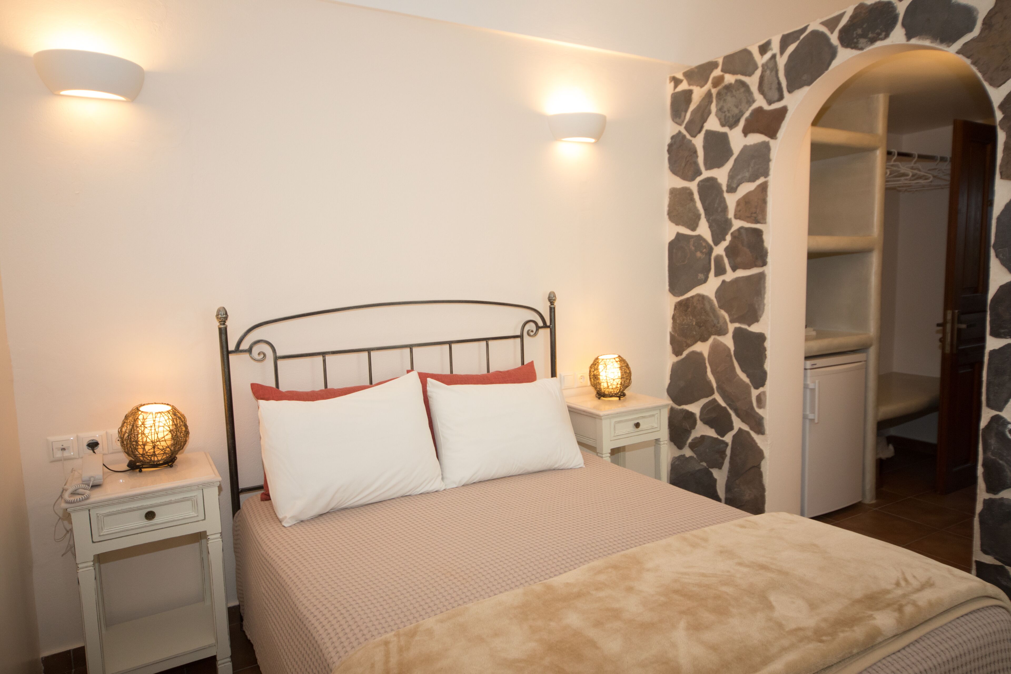 Un dormitorio con cama, lámparas de noche, teléfono y pared de piedra.