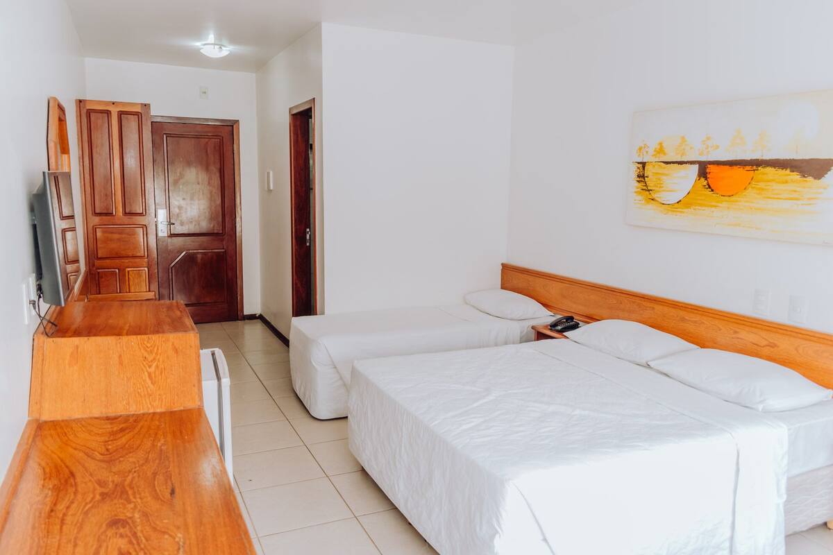 Una habitación de hotel con dos camas individuales, un escritorio de madera, un televisor y un cuadro en la pared.