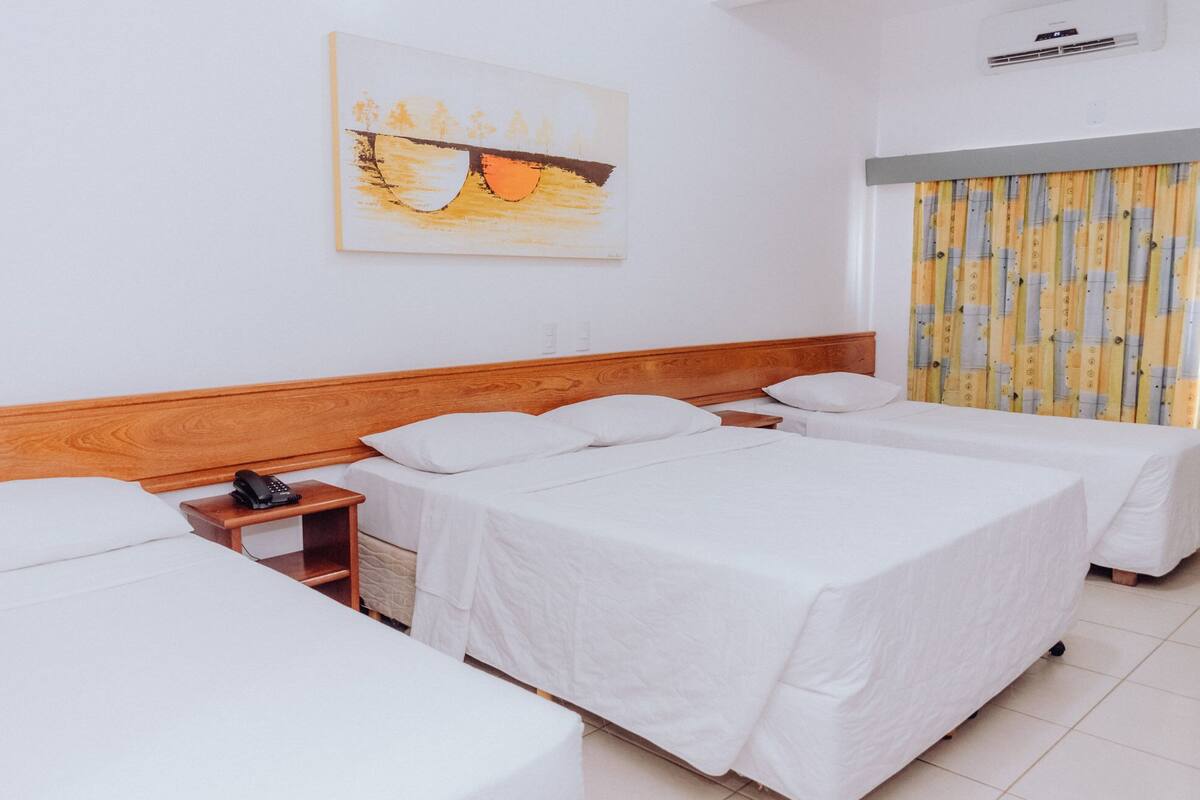Habitación de hotel con dos camas individuales, cabecera de madera, mesita de noche con teléfono y un cuadro en la pared.