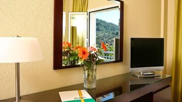 Ein Hotelzimmer mit Schreibtisch, Lampe, Fernseher und einer Vase mit Blumen.
