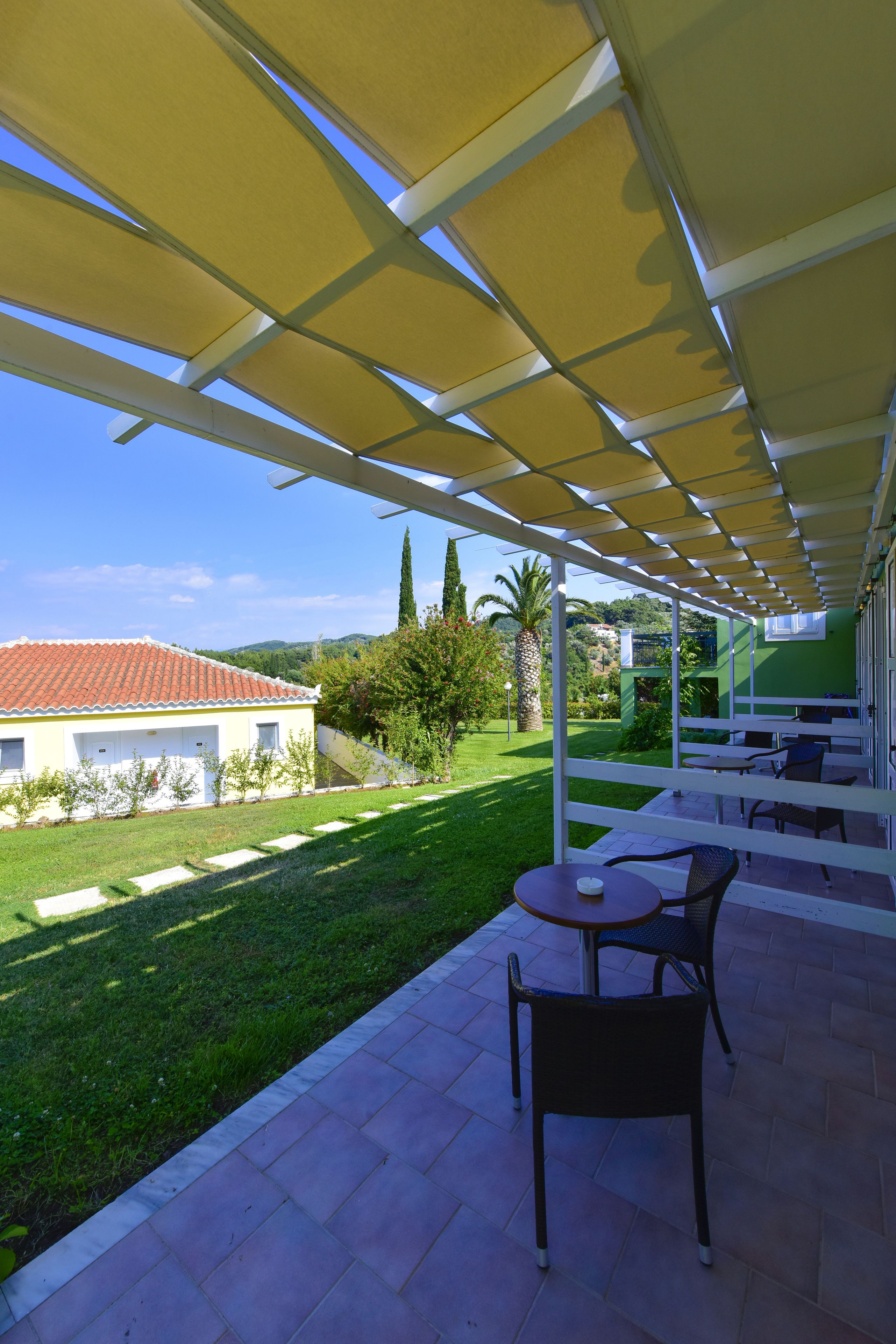 A covered patio area with outdoor seating, a view of a house with a red-tiled roof, and a well-maintained lawn.