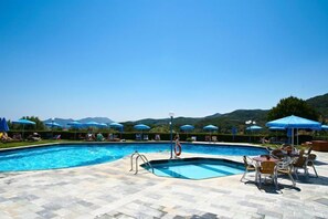 A swimming pool with lounge chairs and umbrellas, surrounded by mountains.