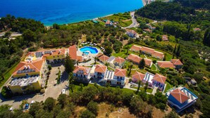 Ovenudblik over et kystnært boligområde med swimmingpool, flere huse og en vej, der fører til havet.