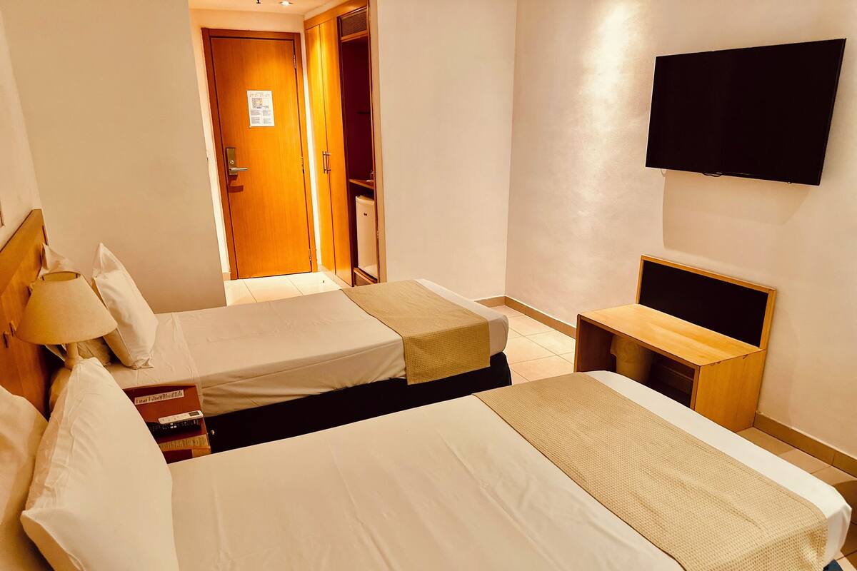 Ein Hotelzimmer mit zwei Betten, einem Fernseher, einem Schreibtisch und einem Kleiderschrank.