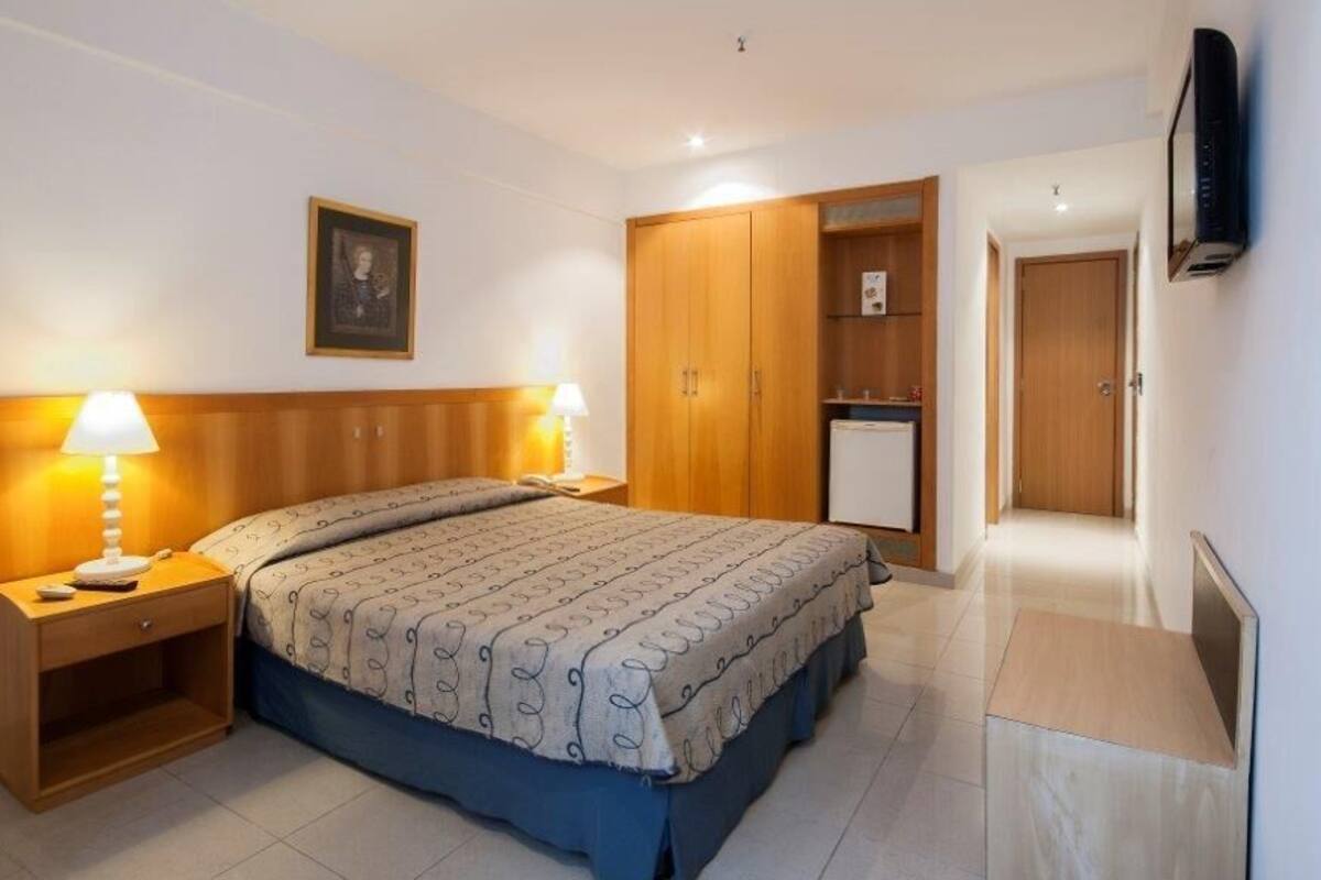 Ein Schlafzimmer mit Bett, Nachttischlampen, einem Kleiderschrank, einem Fernseher und einer kleinen Küchenzeile.