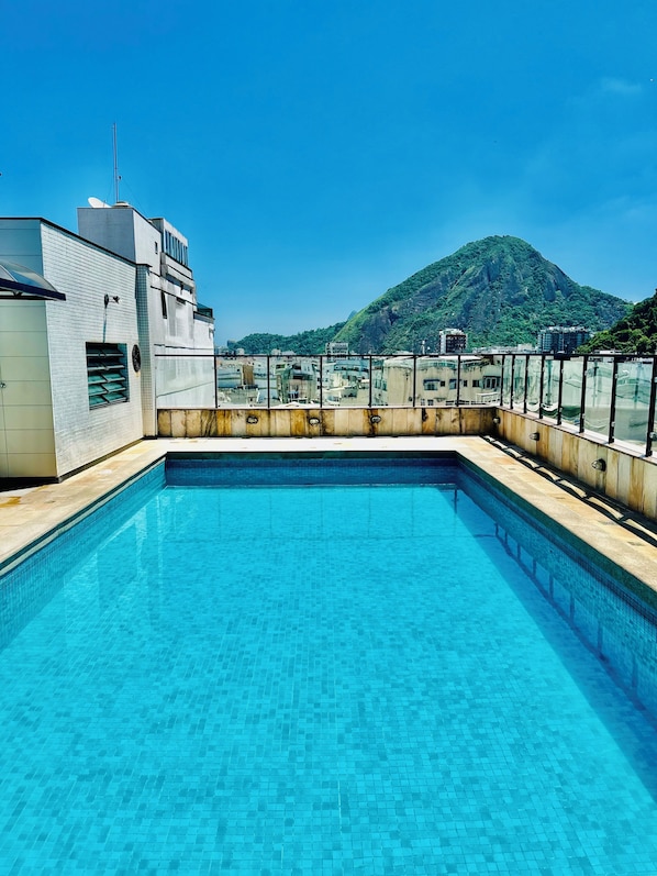Una piscina en la azotea con agua cristalina, rodeada de edificios y una montaña al fondo.