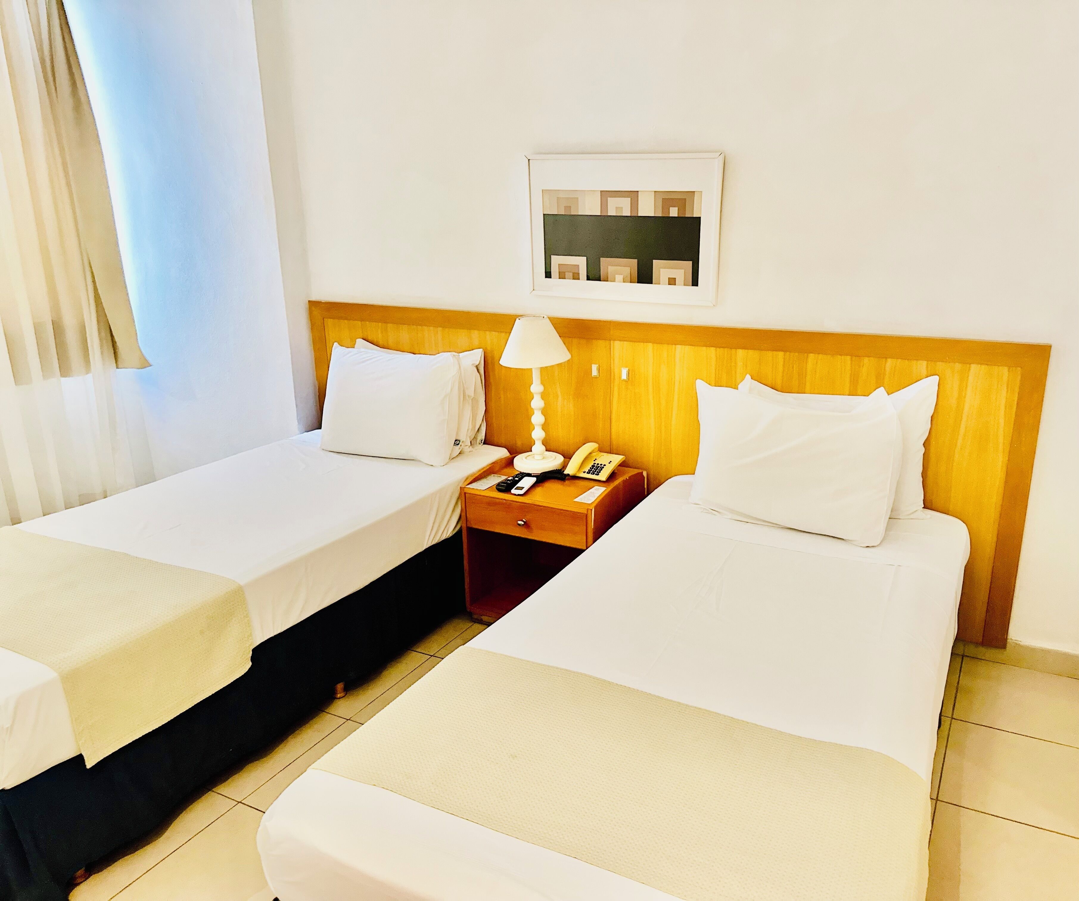 Habitación de hotel con dos camas, una mesita de noche con lámpara, teléfono y un cuadro en la pared.