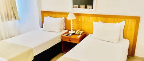 Habitación de hotel con dos camas, una mesita de noche con lámpara, teléfono y un cuadro en la pared.
