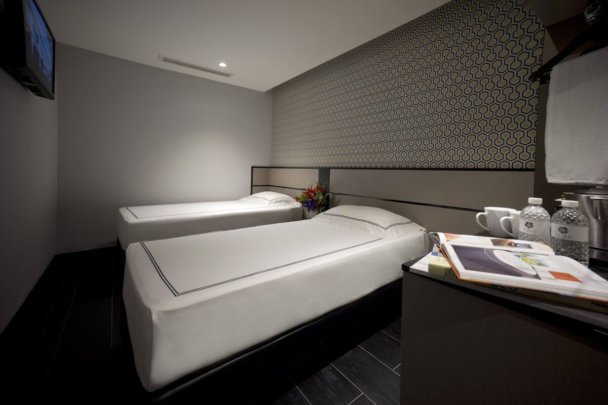 Une chambre d’hôtel moderne avec deux lits simples, une petite salle de bain et un comptoir avec des articles de toilette.