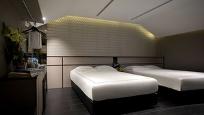 Une chambre d’hôtel moderne équipée de deux lits simples, d’un bureau avec un ordinateur et d’un panneau décoratif mural.
