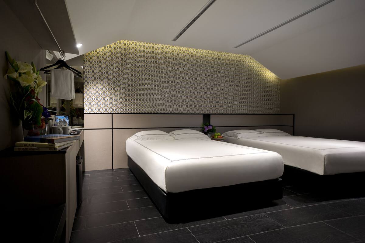 Une chambre d’hôtel moderne équipée de deux lits simples, d’un bureau avec un ordinateur et d’un panneau décoratif mural.