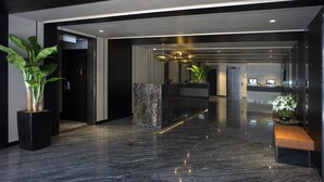 Un hall d’entrée moderne avec un comptoir de réception en marbre, une plante en pot, un banc et un espace d’accueil doté d’un téléviseur.