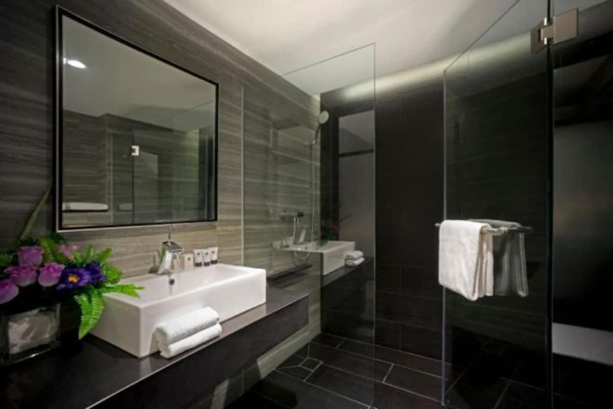 Une salle de bain moderne avec un grand miroir, un lavabo blanc et une cabine de douche en verre.