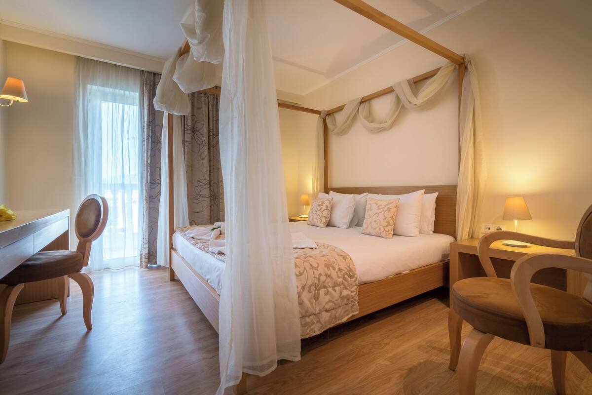 A bedroom with a canopy bed, wooden furniture, and a desk with a lamp.