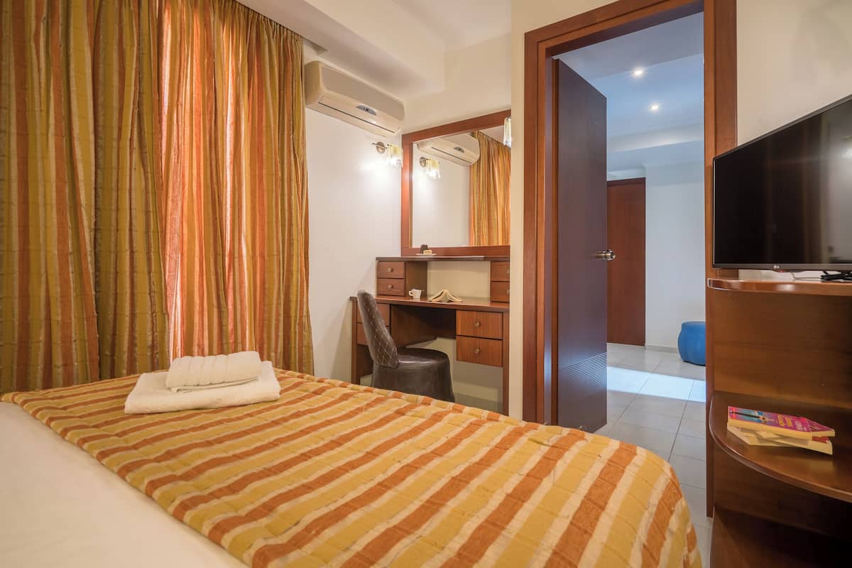 A hotel room with a bed, a desk, a chair, a television, and a wardrobe.