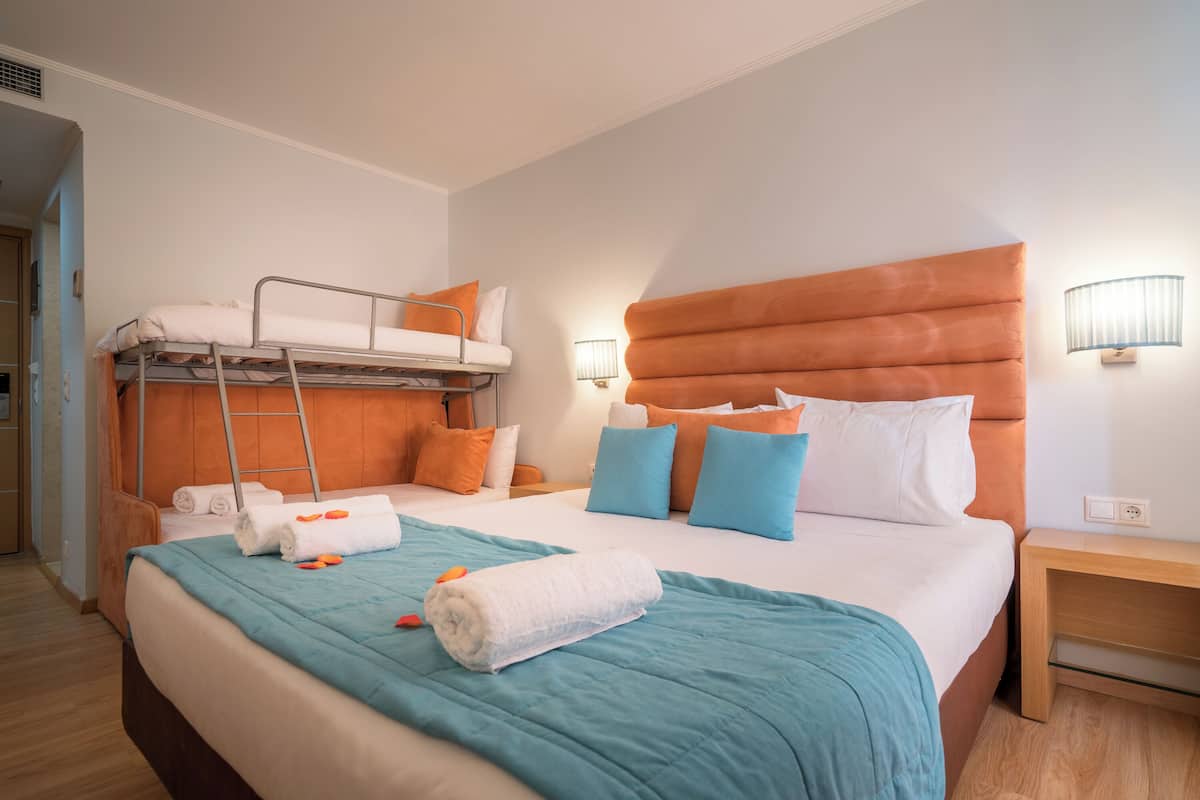 A hotel room with a bunk bed, a large bed with a teal bedspread, and a wooden nightstand.