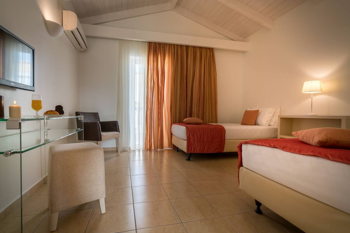 A hotel room with a bed, a desk, a chair, a glass table, a lamp, and a window with curtains.