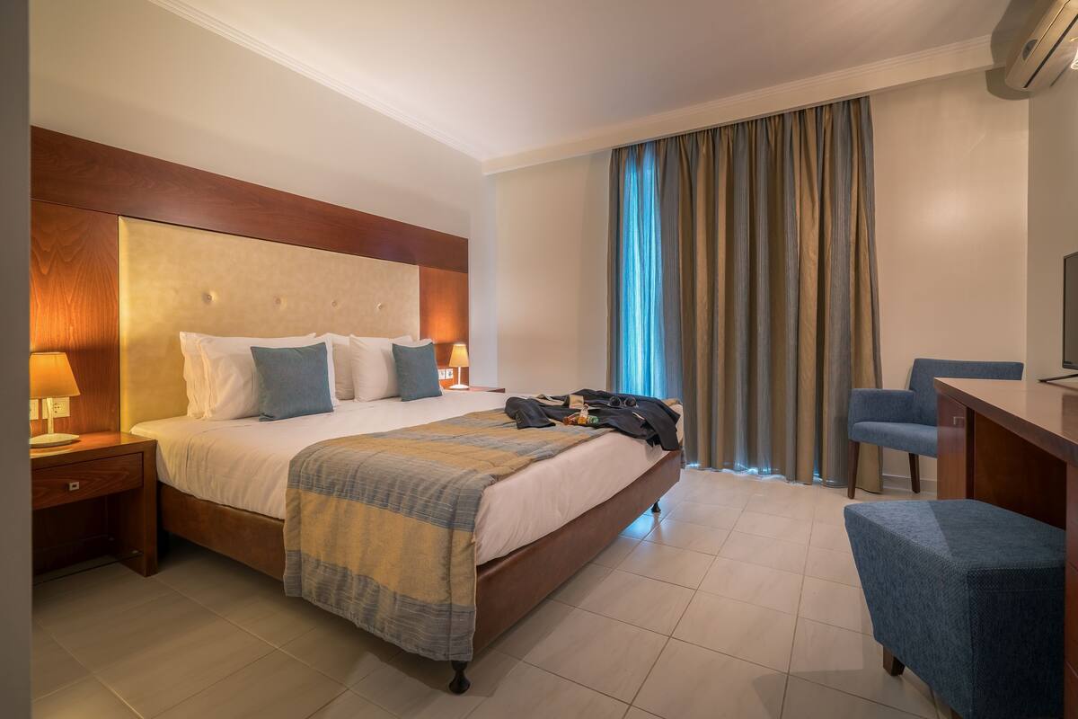 A hotel room with a large bed, a desk, a chair, and a TV.