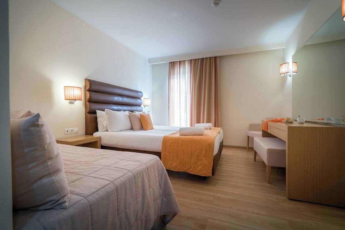 A hotel room with two beds, a desk, a chair, and a large mirror.