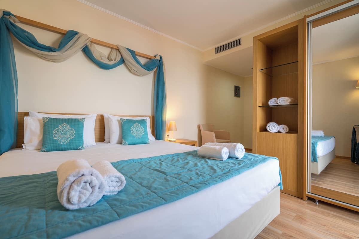 A hotel room with a large bed, a wardrobe, and a mirror.