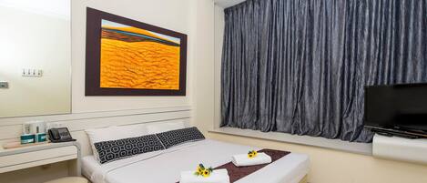 Een hotelkamer met een bed, een bureau met telefoon, een koffieapparaat en een televisie.