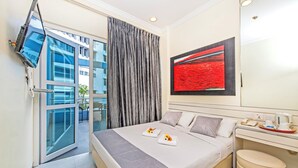 Een moderne hotelkamer met een bed, bureau, flatscreen-tv aan de muur en een groot raam met gordijnen.