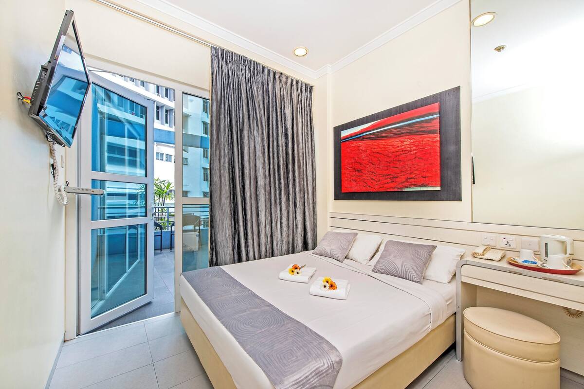 Een moderne hotelkamer met een bed, bureau, flatscreen-tv aan de muur en een groot raam met gordijnen.