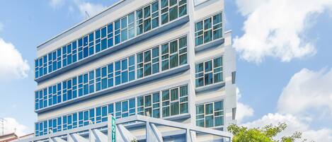 Un hotel moderno con una estructura de varios pisos, amplias ventanas y un área de entrada cubierta.