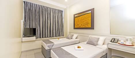 A hotel room with two beds, a desk, a TV, and a large window with curtains.