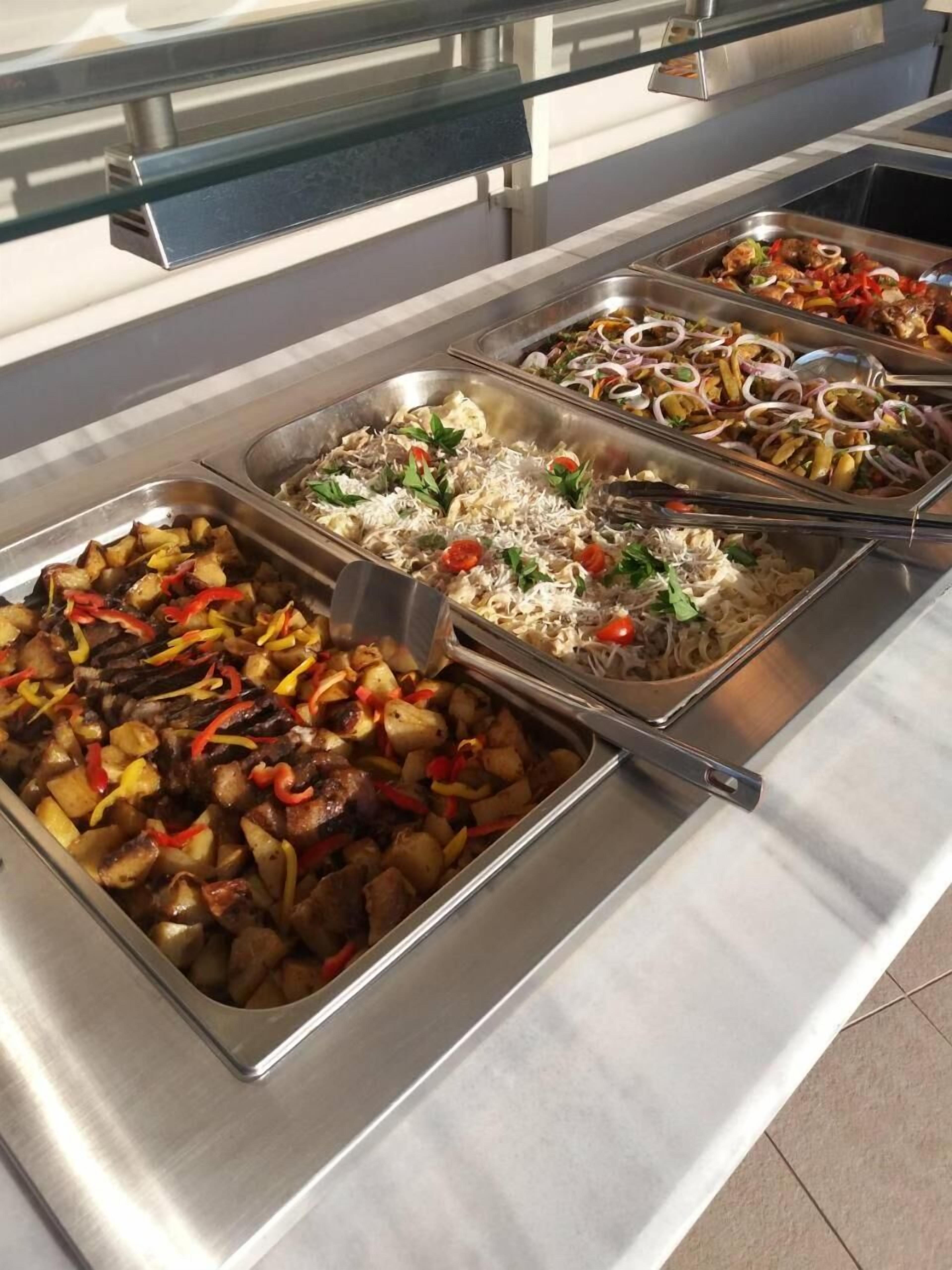 Un buffet proposant une variété de plats, notamment des légumes rôtis, des pâtes et des fruits de mer.