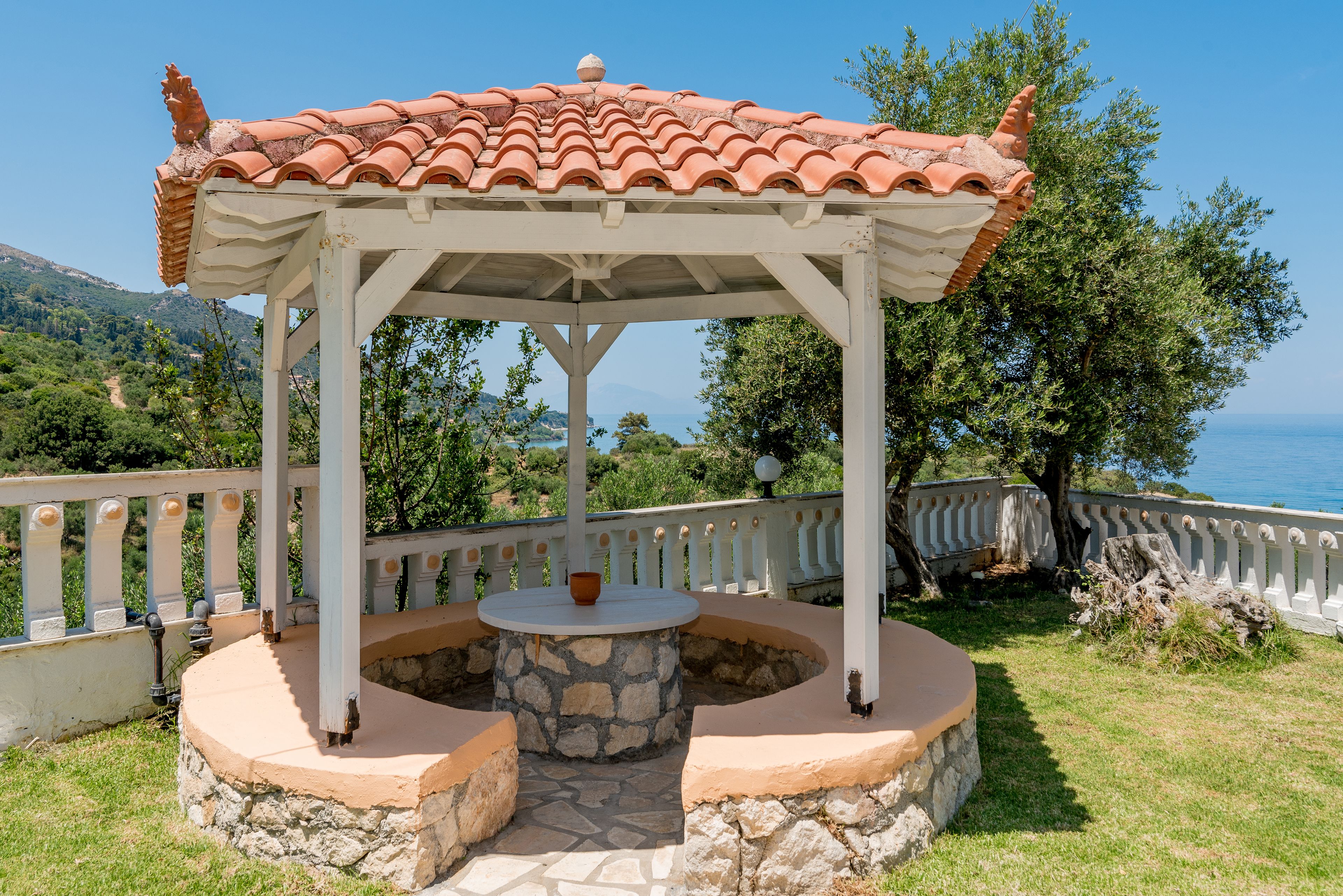 A gazebo with a tiled roof, stone base, and a table with a cup.